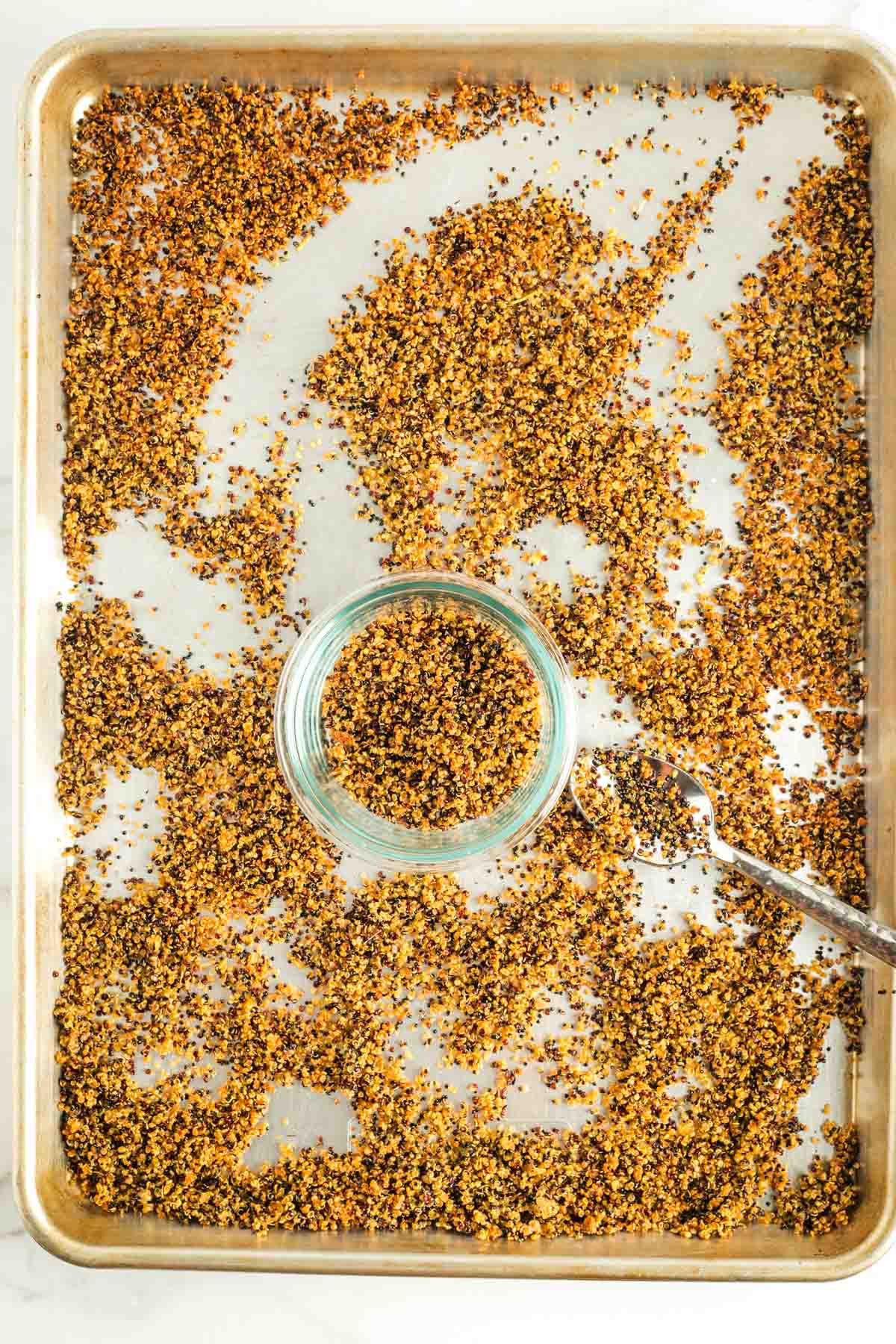 Spooning crispy quinoa into a bowl from a baking sheet. 