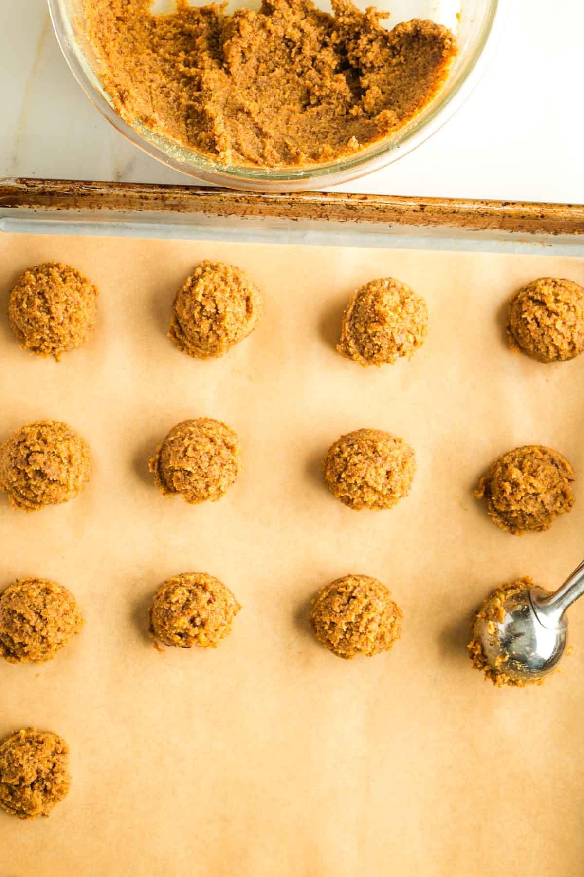 A cookie scoop dropping portions of pumpkin cookie dough onto a baking sheet. 