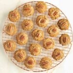 Pumpkin thumbprint cookies filled with salted caramel and a pecan cooling on a wire rack.