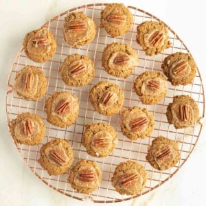 Pumpkin thumbprint cookies filled with salted caramel and a pecan cooling on a wire rack.
