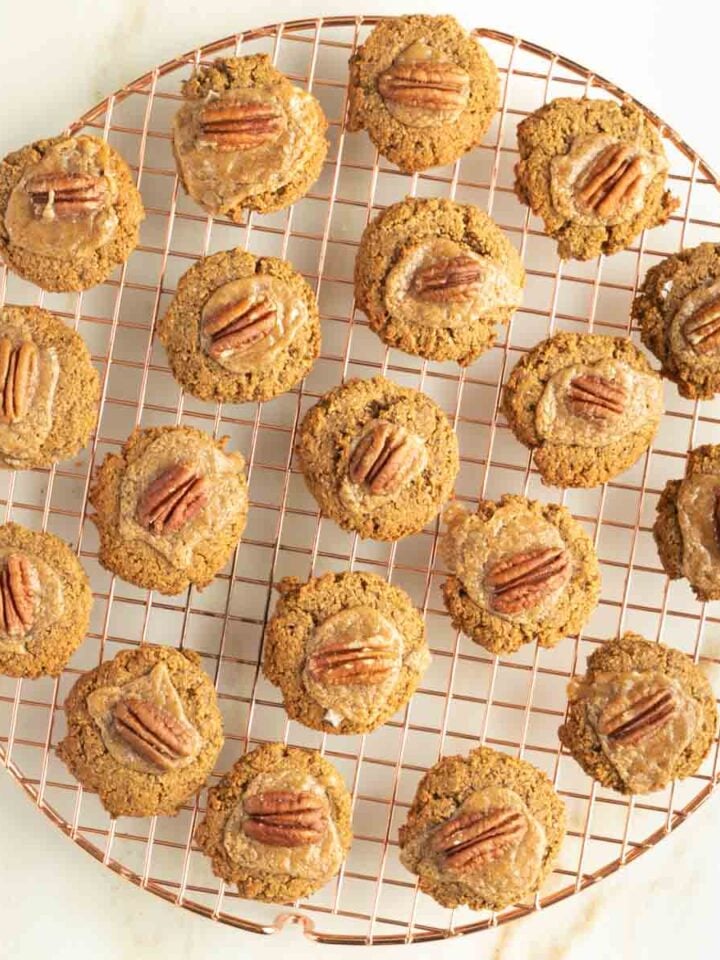 Pumpkin thumbprint cookies filled with salted caramel and a pecan cooling on a wire rack.