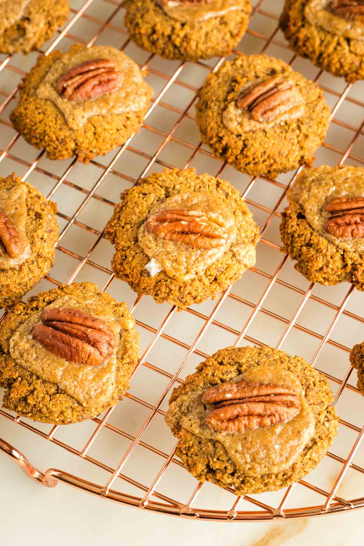 Pumpkin thumbprint cookies filled with caramel and topped with a pecan, cooling on a wire rack. 