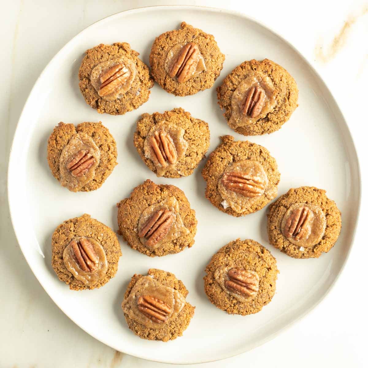 Plate of pumpkin thumbprint cookies filled with salted caramel and pecans. 