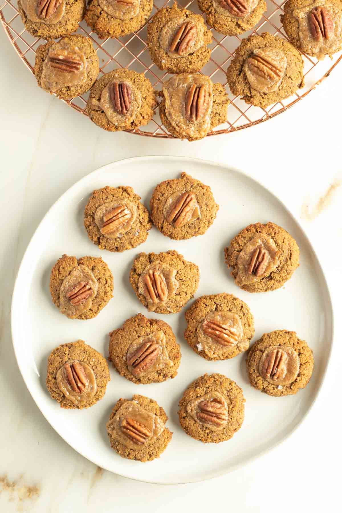 Plate of pumpkin thumbprint cookies with tahini caramel center topped with a pecan.