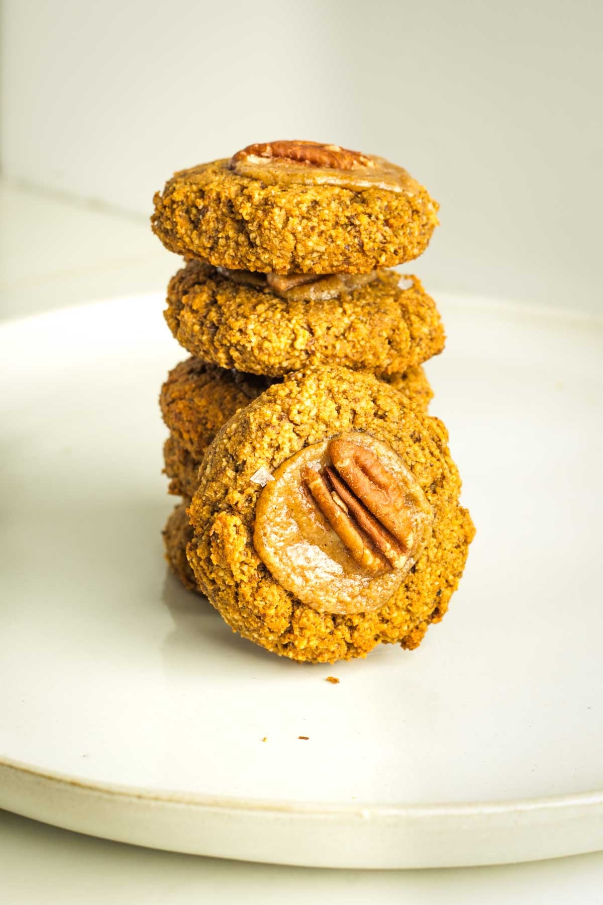 Stack of pumpkin cookies with one on its side so you can see the caramel filling and pecan on top. 