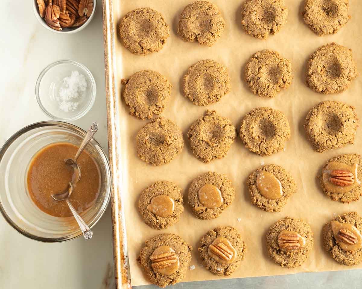 Using two spoons to put caramel filling inside the cavity of a pumpkin cookie.
