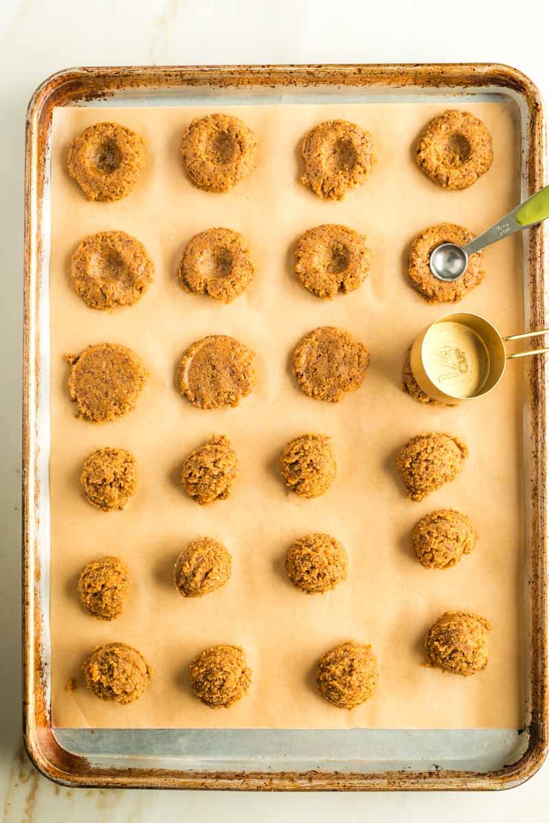 Pressing down pumpkin cookie dough balls with the back of a measuring cup and then indenting them with a ¼ teaspoon measuring spoon. 