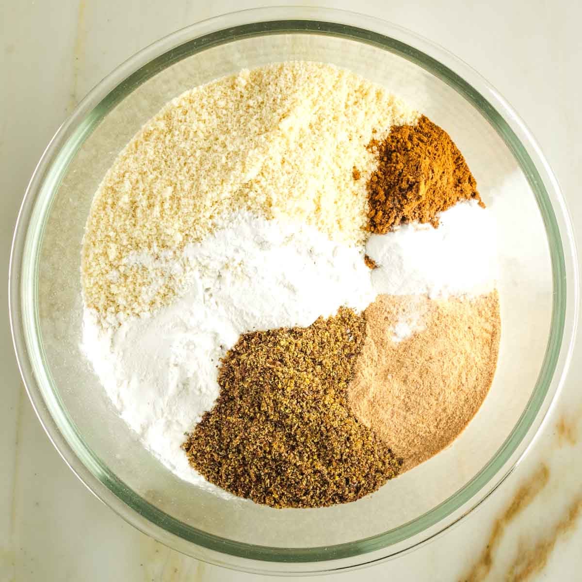Dry ingredients in a bowl including pumpkin pie spice, almond flour, arrowroot powder, ground flax, date sugar and baking powder. 