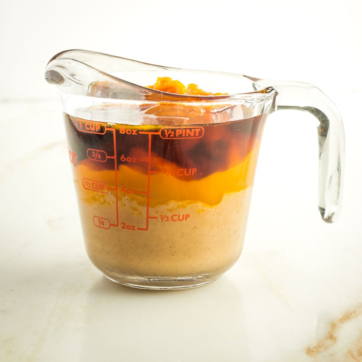 Wet ingredients in a pyrex measuring cup including pumpkin puree, tahini and maple syrup.