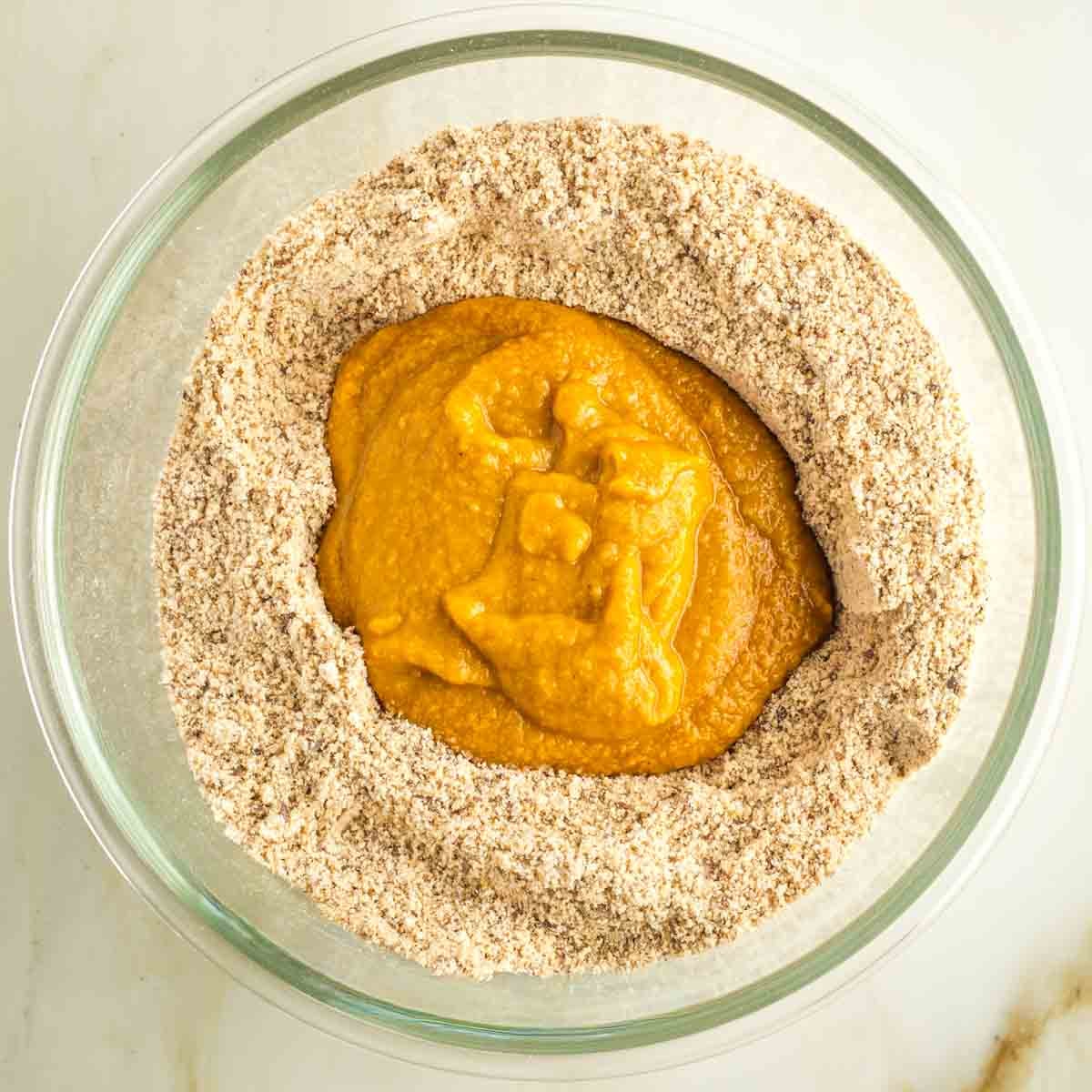 Pumpkin mixture on top of dry ingredients in a glass mixing bowl. 
